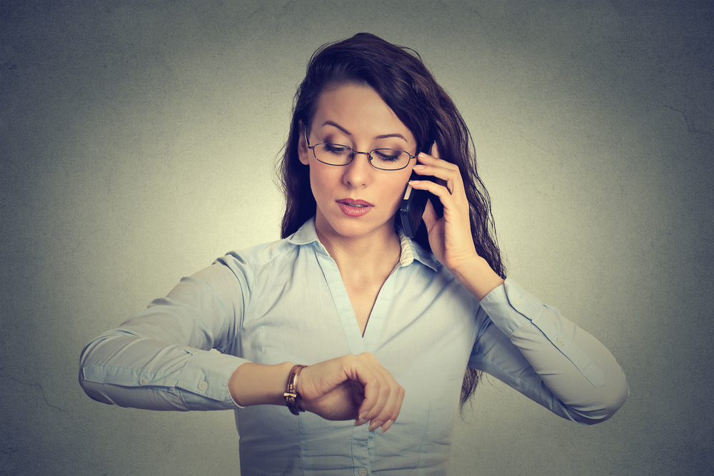 Business and time management concept. Young businesswoman looking at wrist watch, talking on mobile phone running late for meeting. Time is money